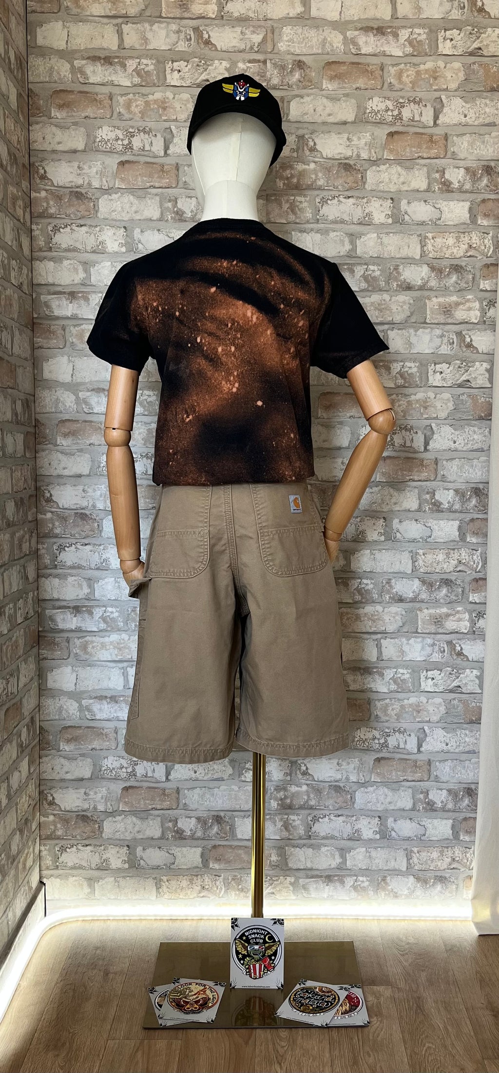 Silhouette streetwear portée par un mannequin avec un t-shirt noir Black Veil Brides, un short carpenter DKH Carhartt, une ceinture en cuir Fossil et une casquette Goldorak , de dos . Patchs La Barbuda au sol