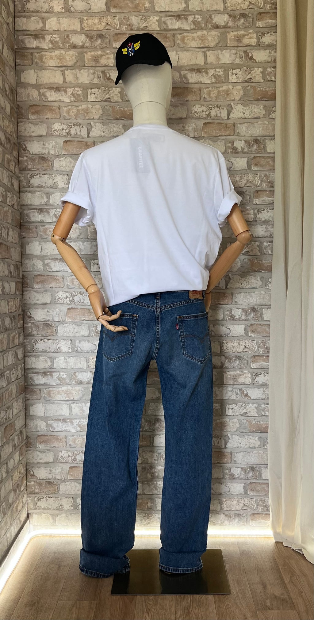 T-Shirt Demogorgon / Parodie Logo Vintage Blanc - XL Grafitee et jJean Levi's 505 Regular Fit Bleu Medium Stonewash - W32 L34 sur un mannequin de dos avec une casquette Grafitee