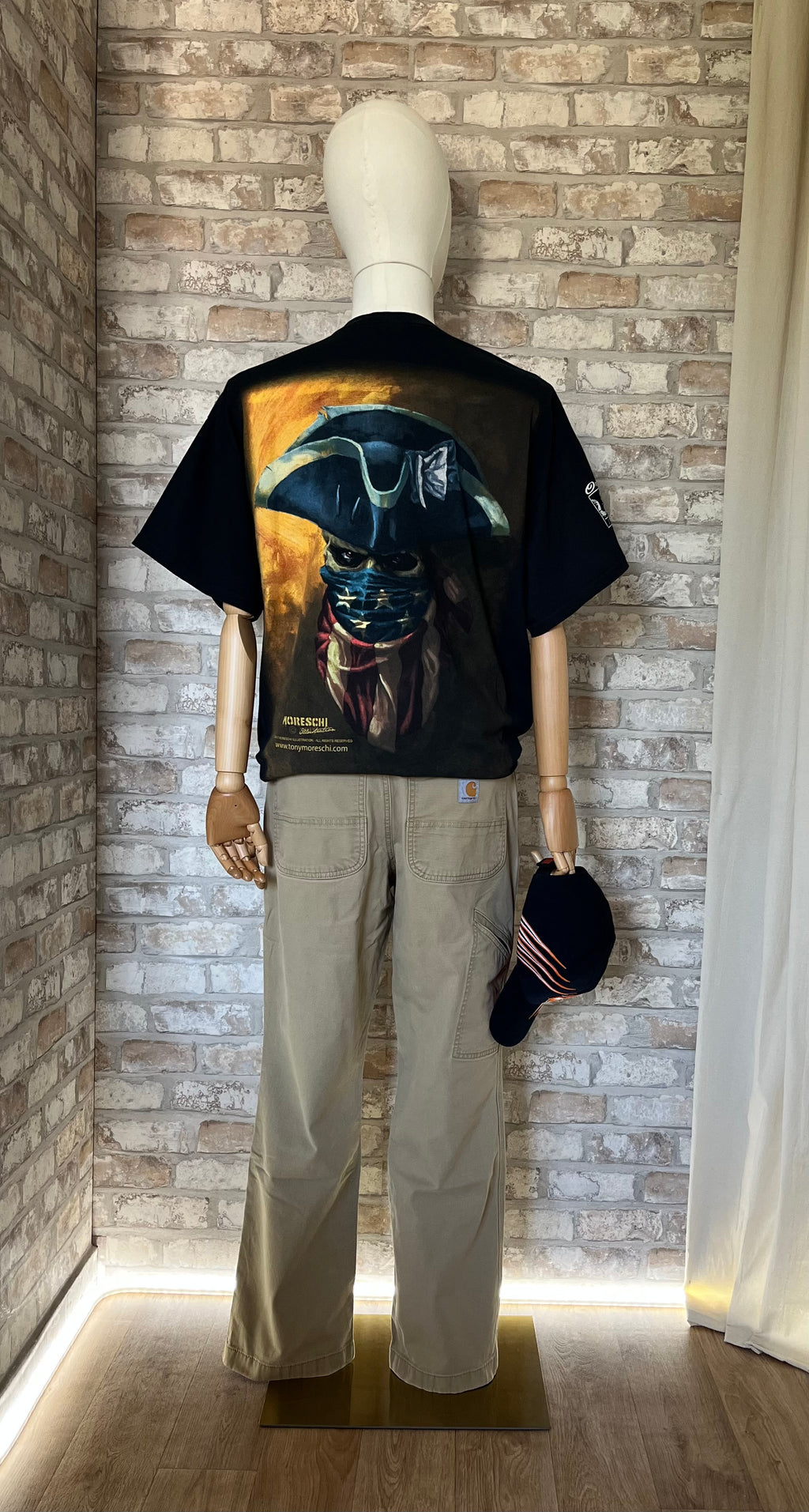 T-Shirt Gildan, Moreschi Illustration, Pirate Skull Flag porté de dos avec un Pantalon Carhartt BN2291, Relaxed Fit, sur un mannequin, avec à la main une casquette vintage Harley Davidson