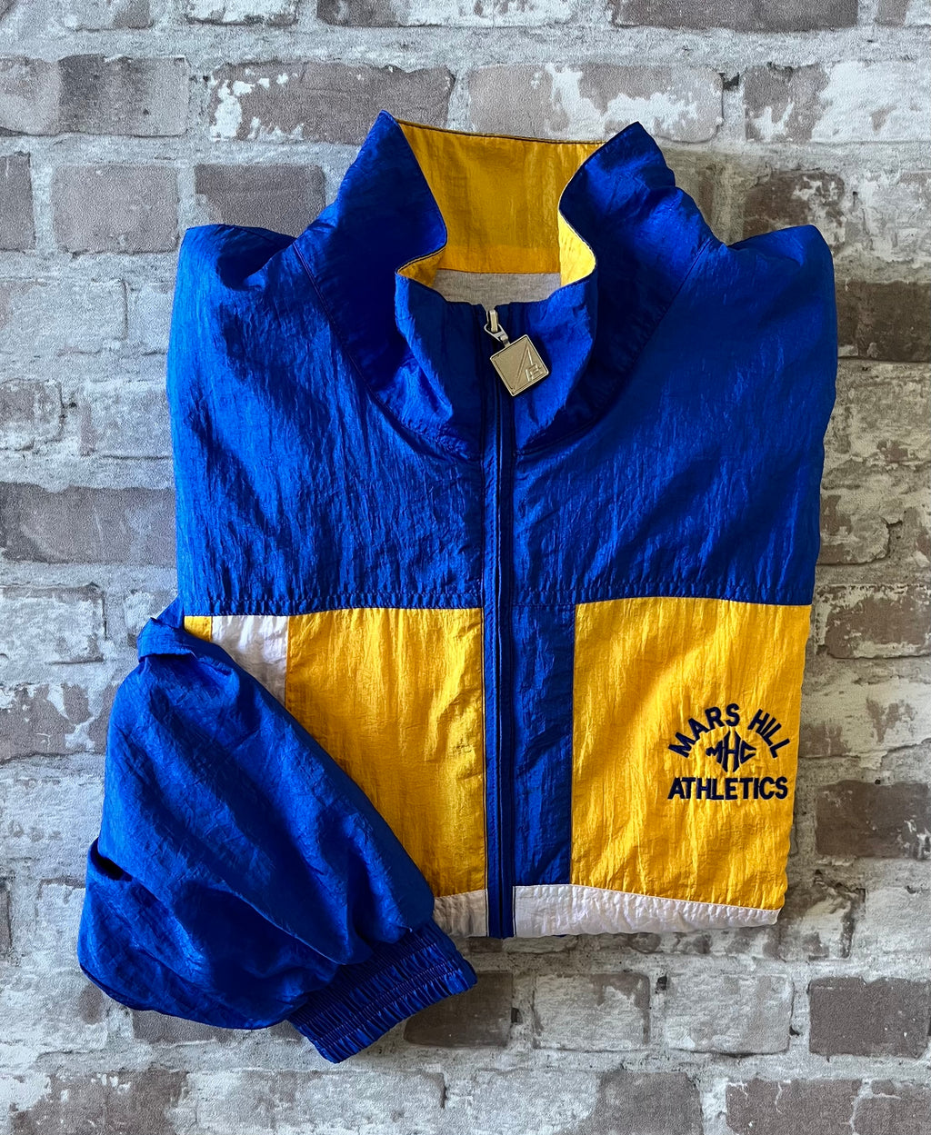 Track jacket américaine des années 90 au design géométrique bleu, jaune et blanc, présentée pliée à plat.