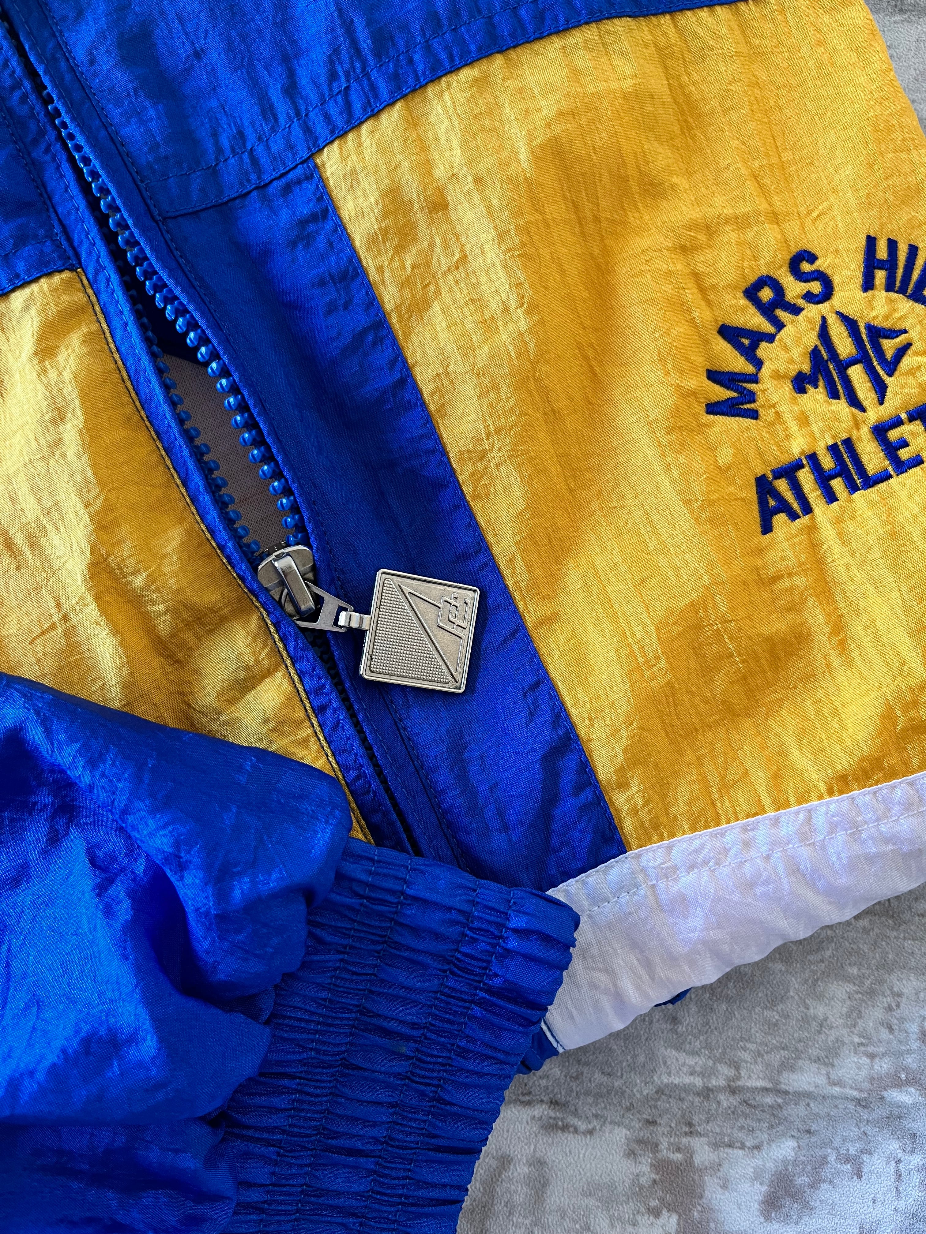 Veste coupe-vent vintage Pro Celebrity colorblock bleu royal et jaune avec broderie Mars Hill Athletics, présentée à plat, focus curseur et broderies.