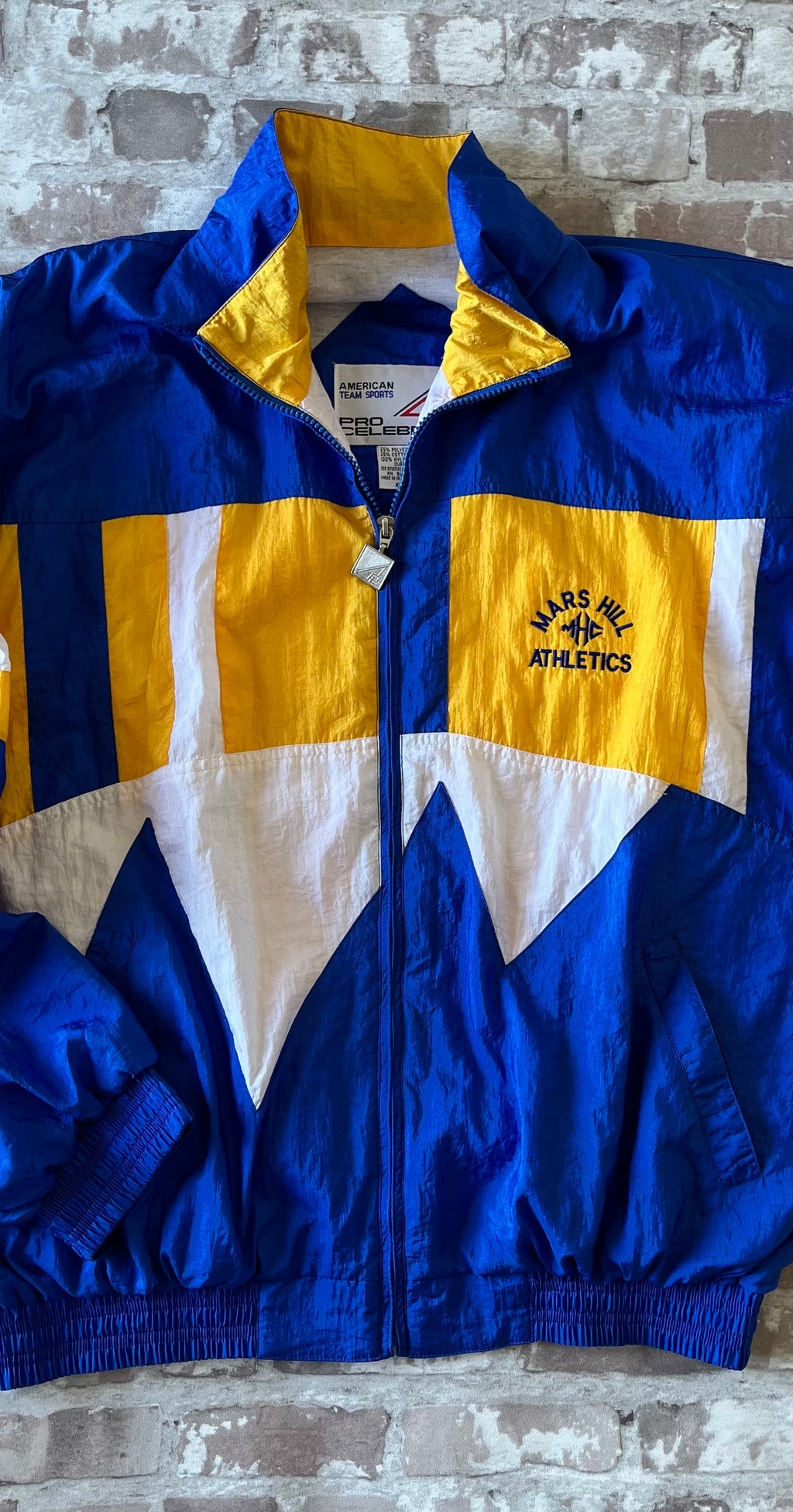 Veste coupe-vent vintage Pro Celebrity colorblock bleu royal et jaune avec broderie Mars Hill Athletics, présentée à plat.
