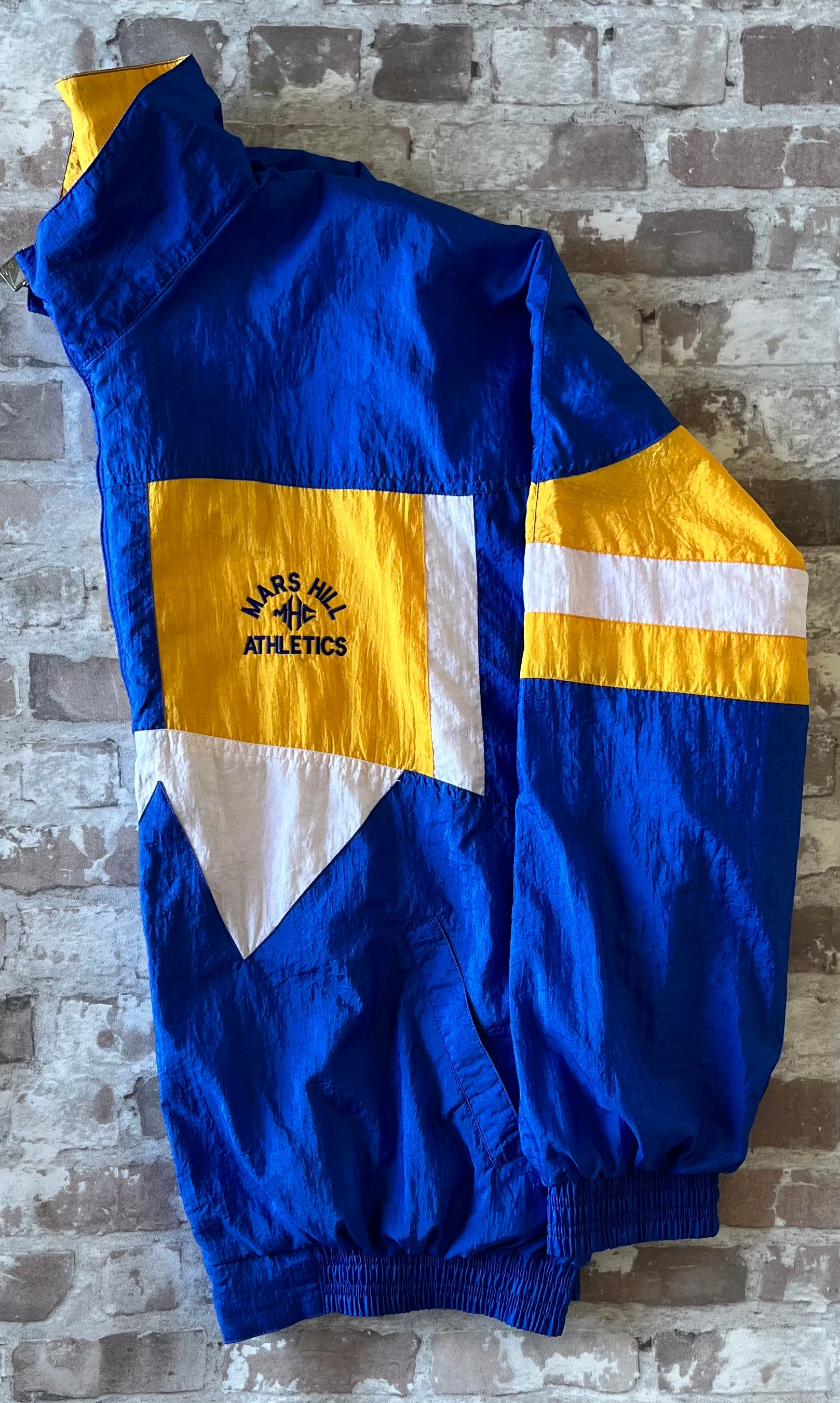 Veste coupe-vent vintage Pro Celebrity colorblock bleu royal et jaune avec broderie Mars Hill Athletics, présentée à plat.
