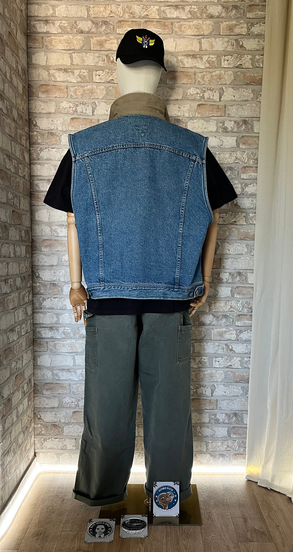 Veste en Jean Tommy Hilfiger Vintage, Sans manches , des 90s, exposée de face sur un mannequin , de dos, avec un pantalon Carhartt, un t-shirt noir, une casquette Grafitee Goldorak et au sol des Patchs La Barbuda , posés.