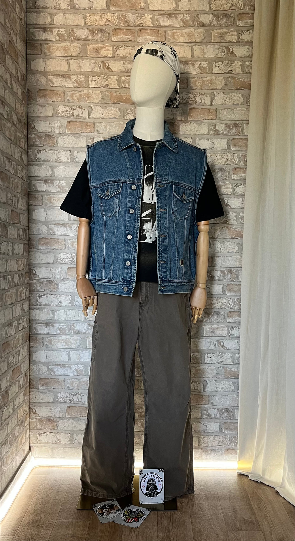 Veste en Jean Tommy Hilfiger Vintage, Sans manches , des 90s, exposée de face sur un mannequin , de face, avec un pantalon Carhartt, unn T-Shirt Vintage SBRBN Dee Dee Ramone RIP 2002 The Ramones, une casquette vintage Adidas et au sol des Patchs La Barbuda , posés.