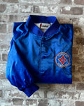 Veste de sport bomber léger rétro Cardinal bleu satiné avec fermeture à boutons-pression et écusson Campers On Mission, présentée à plat, pliée