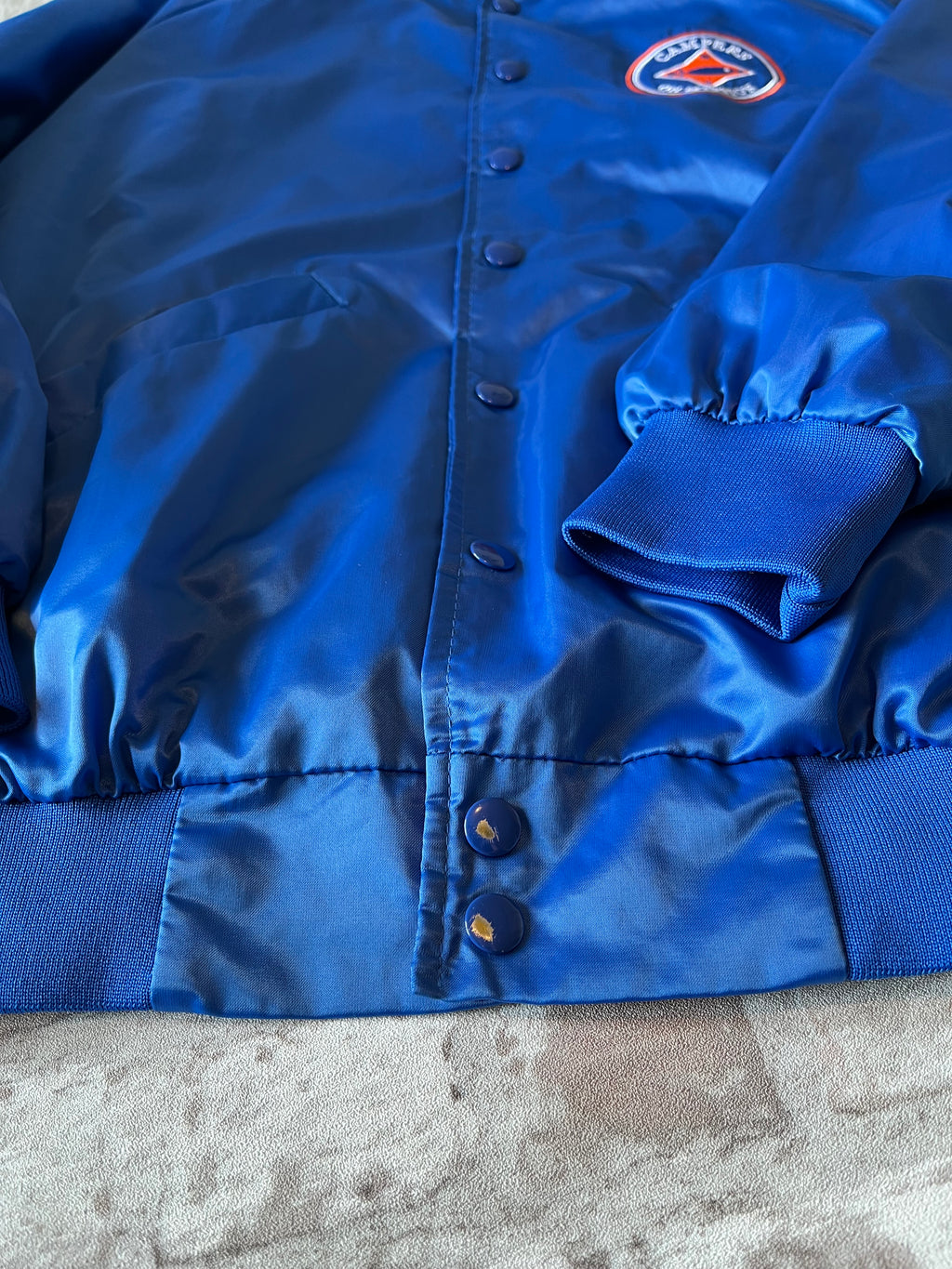 Veste de sport bomber léger rétro Cardinal bleu satiné avec fermeture à boutons-pression et écusson Campers On Mission, présentée à plat, focus boutons sans peinture/patinés