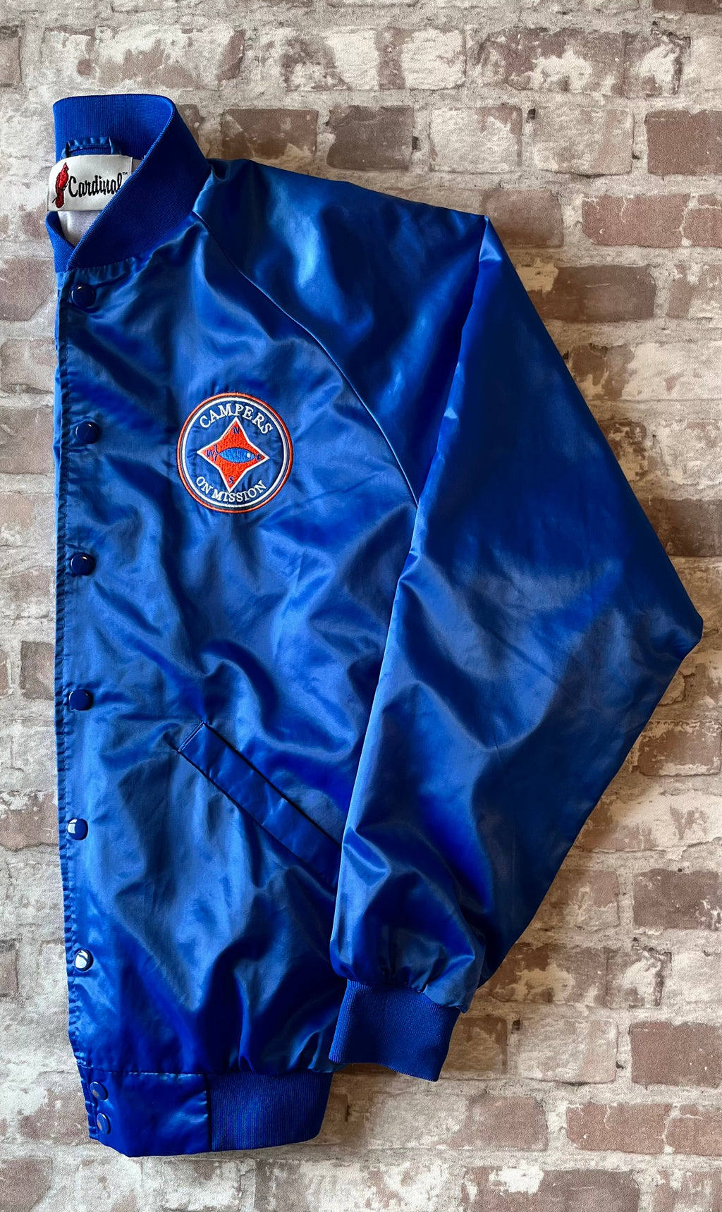 Veste de sport bomber léger rétro Cardinal bleu satiné avec fermeture à boutons-pression et écusson Campers On Mission, présentée à plat, de profil