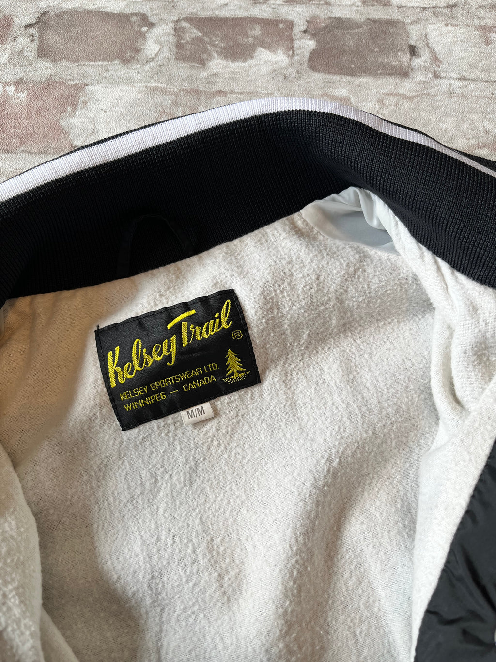 Veste coupe-vent vintage canadienne Kelsey Trail en nylon satiné noir avec boutons-pression et bords-côtes rayés, présentée à plat, focus doublure et étiquette