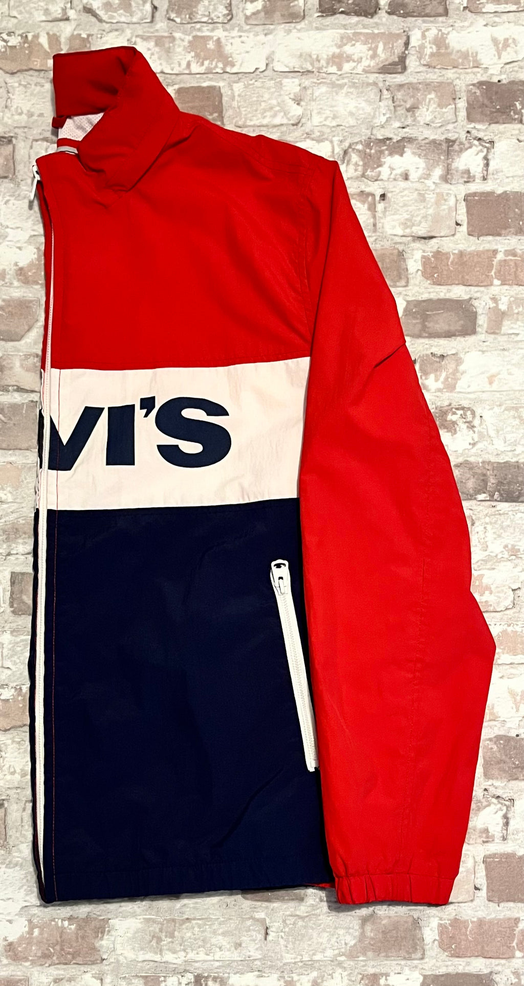 Vue de profil d'une veste de sport rétro Levi's avec col montant et détails de zips blancs contrastés, présentée à plat.
