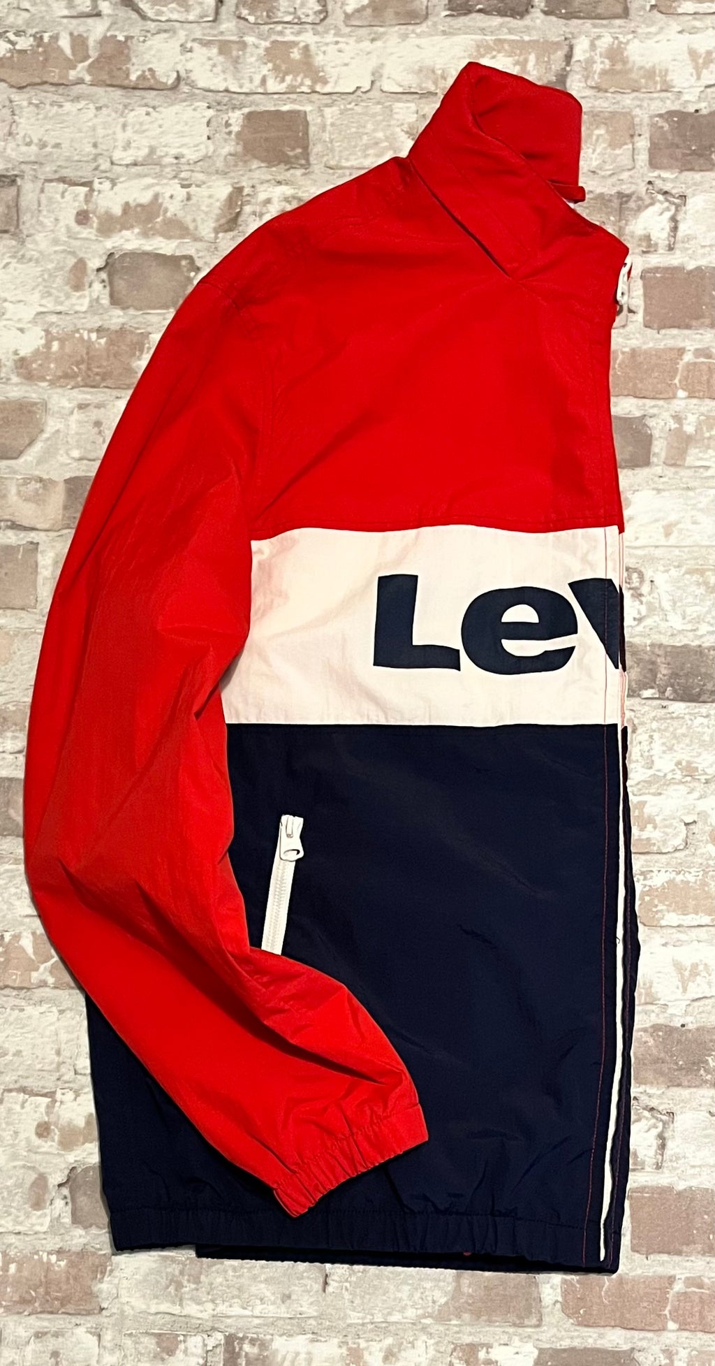 Vue de profil d'une veste de sport rétro Levi's avec col montant et détails de zips blancs contrastés, présentée à plat.