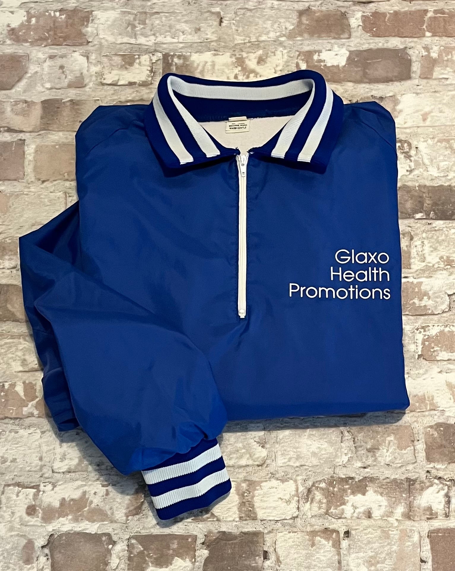 Veste de sport pullover vintage Glaxo bleu roi avec col polo zippé, bords-côtes rayés et sérigraphie sur la poitrine, présentée à plat, pliée