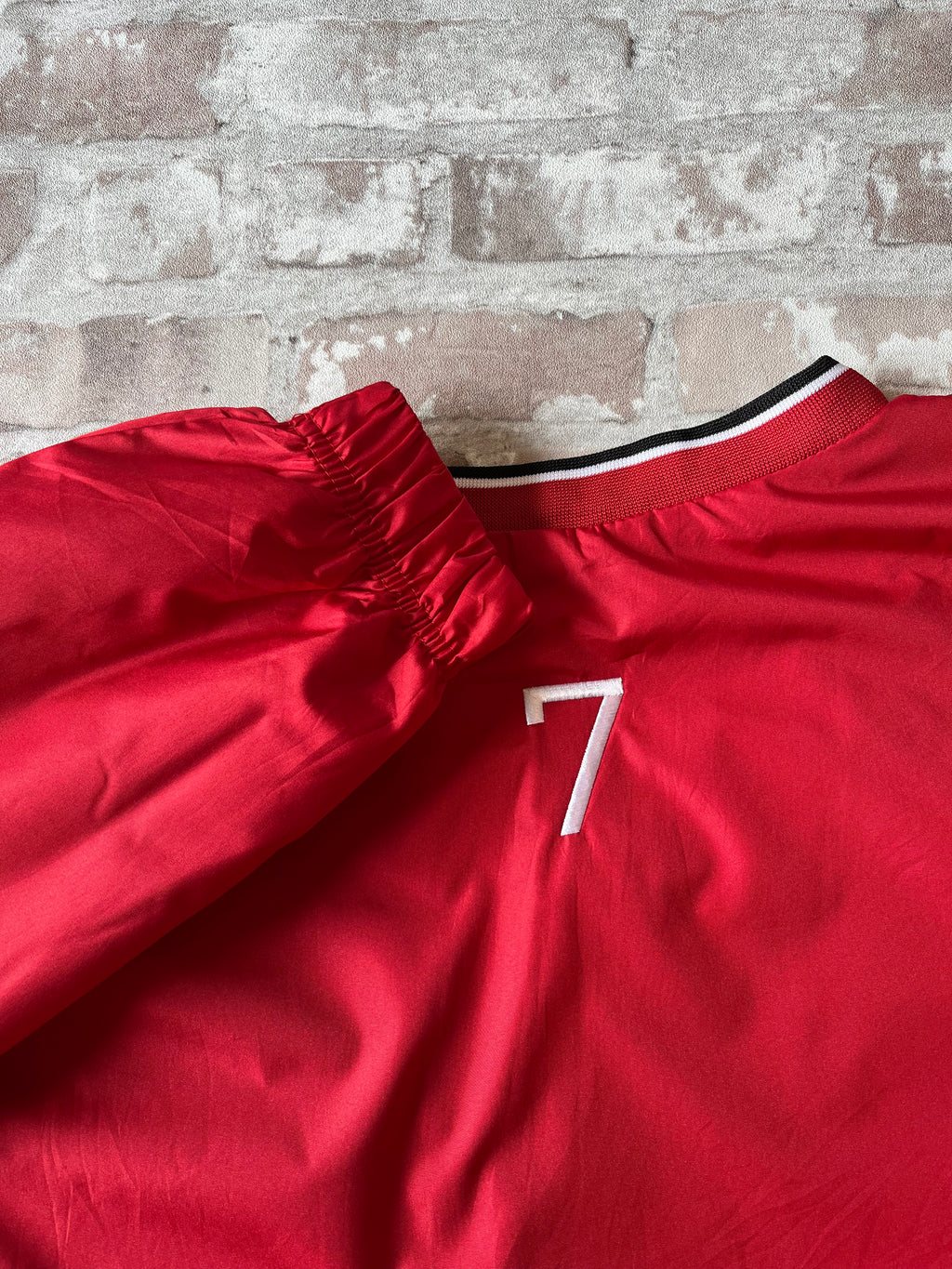 Flocage vintage du numéro 7 noir au dos d'un coupe-vent de football américain des années 2000, présenté plié à plat.
