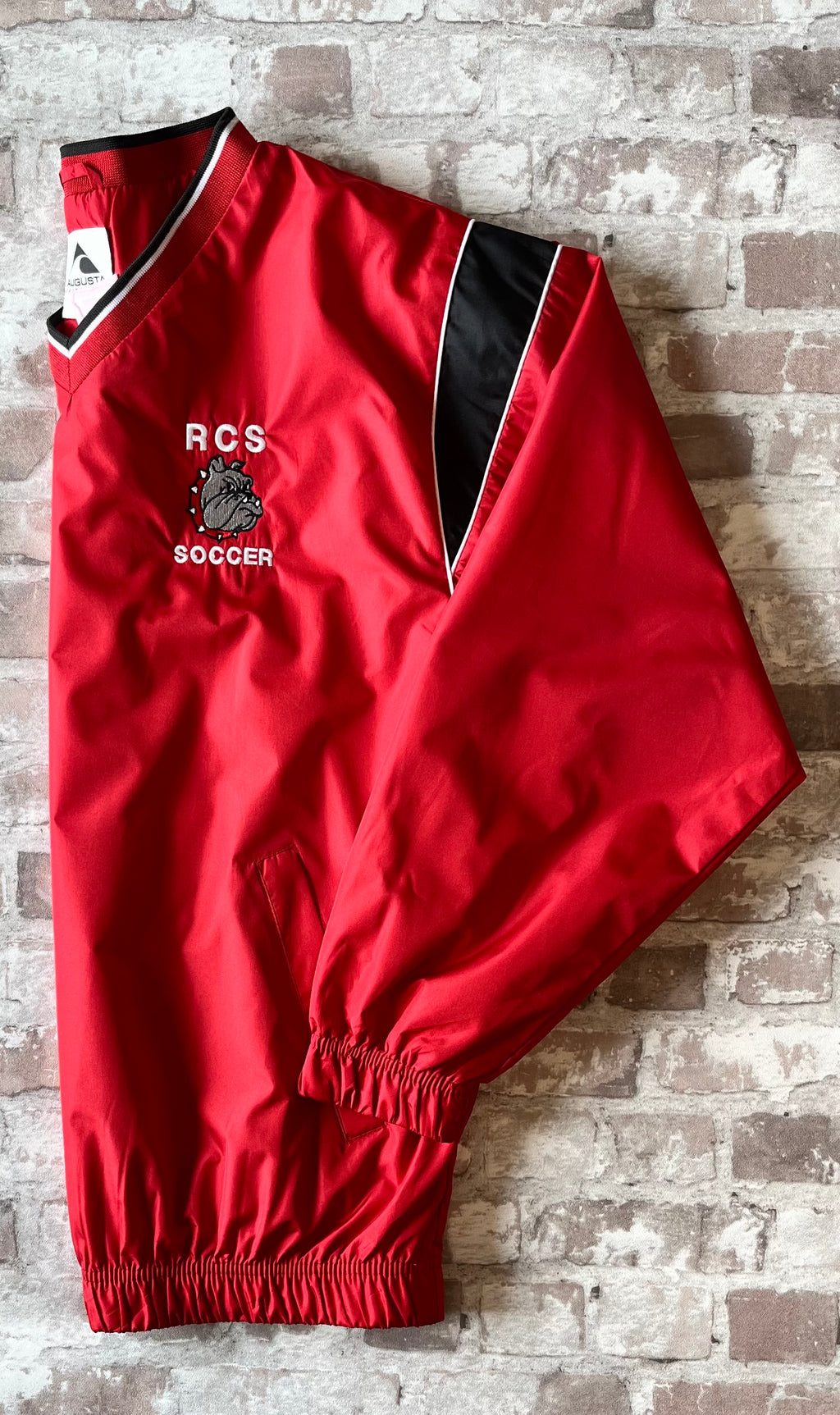 Veste de sport pullover rétro Augusta Sportswear rouge vif avec col en V en maille et logo Bulldog brodé, présentée pliée à plat de profil