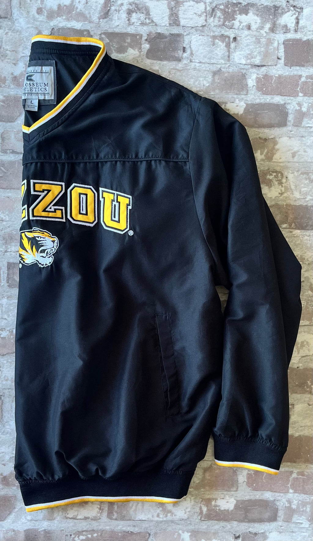 Veste de sport pullover vintage Colosseum Athletics noire avec broderie jaune Mizzou et col en V tricolore, présentée de profil à plat.
