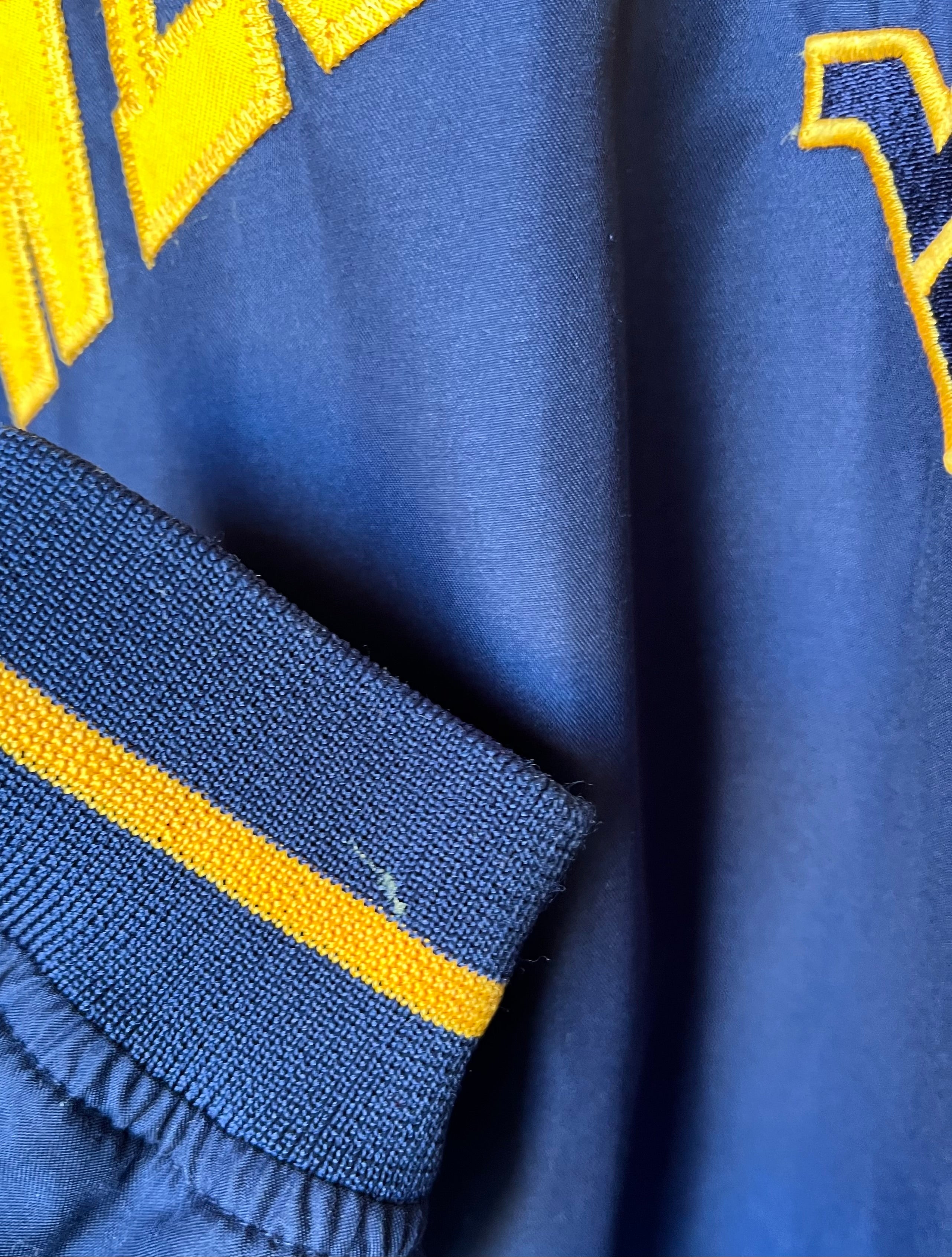 Veste de sport pullover rétro Pro Edge bleu marine avec broderie jaune West Virginia et col en V, présentée pliée à plat / focus tache de colle au poignet