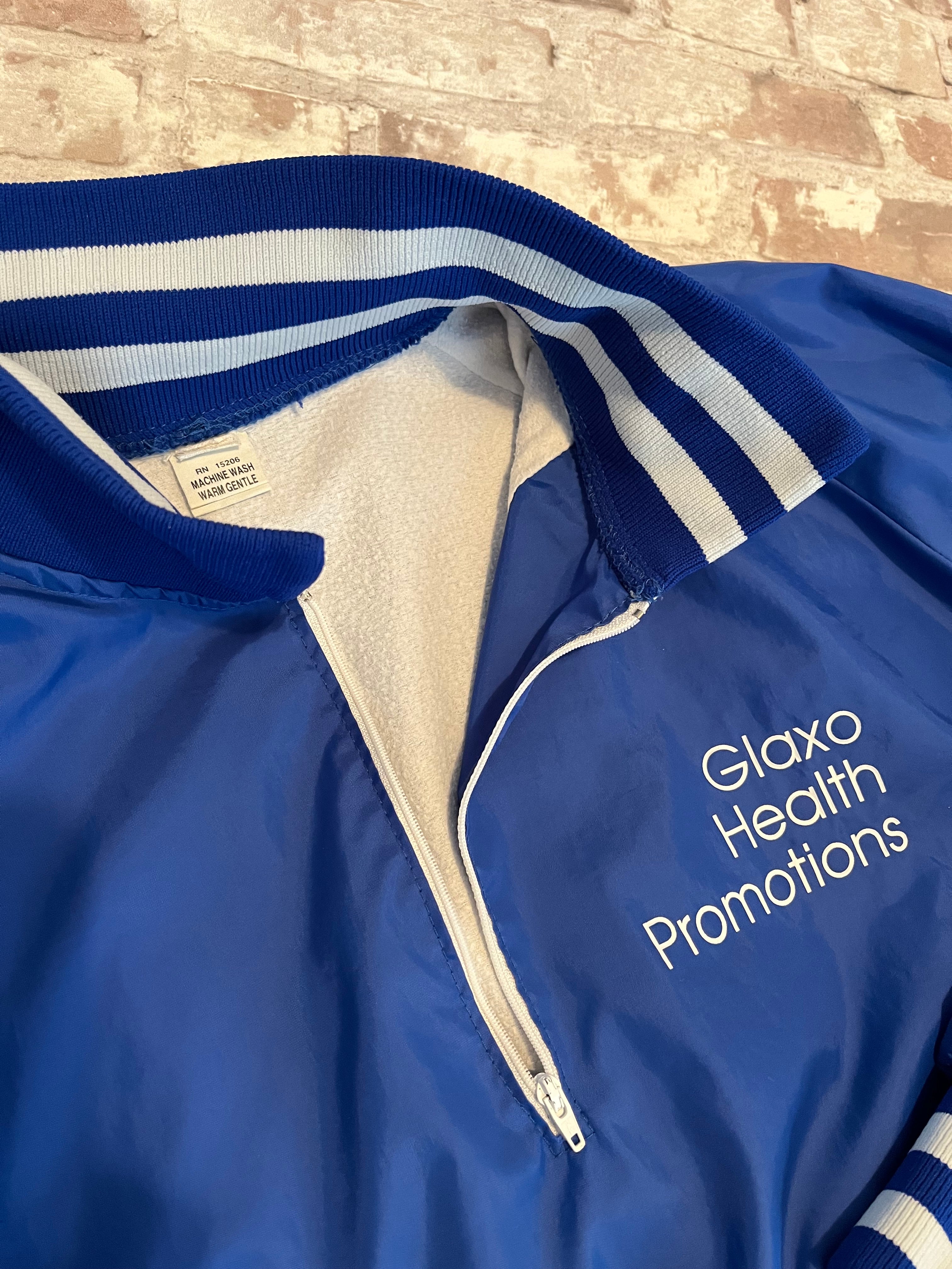 Veste de sport pullover vintage Glaxo bleu roi avec col polo zippé, bords-côtes rayés et sérigraphie sur la poitrine, présentée à plat. 
