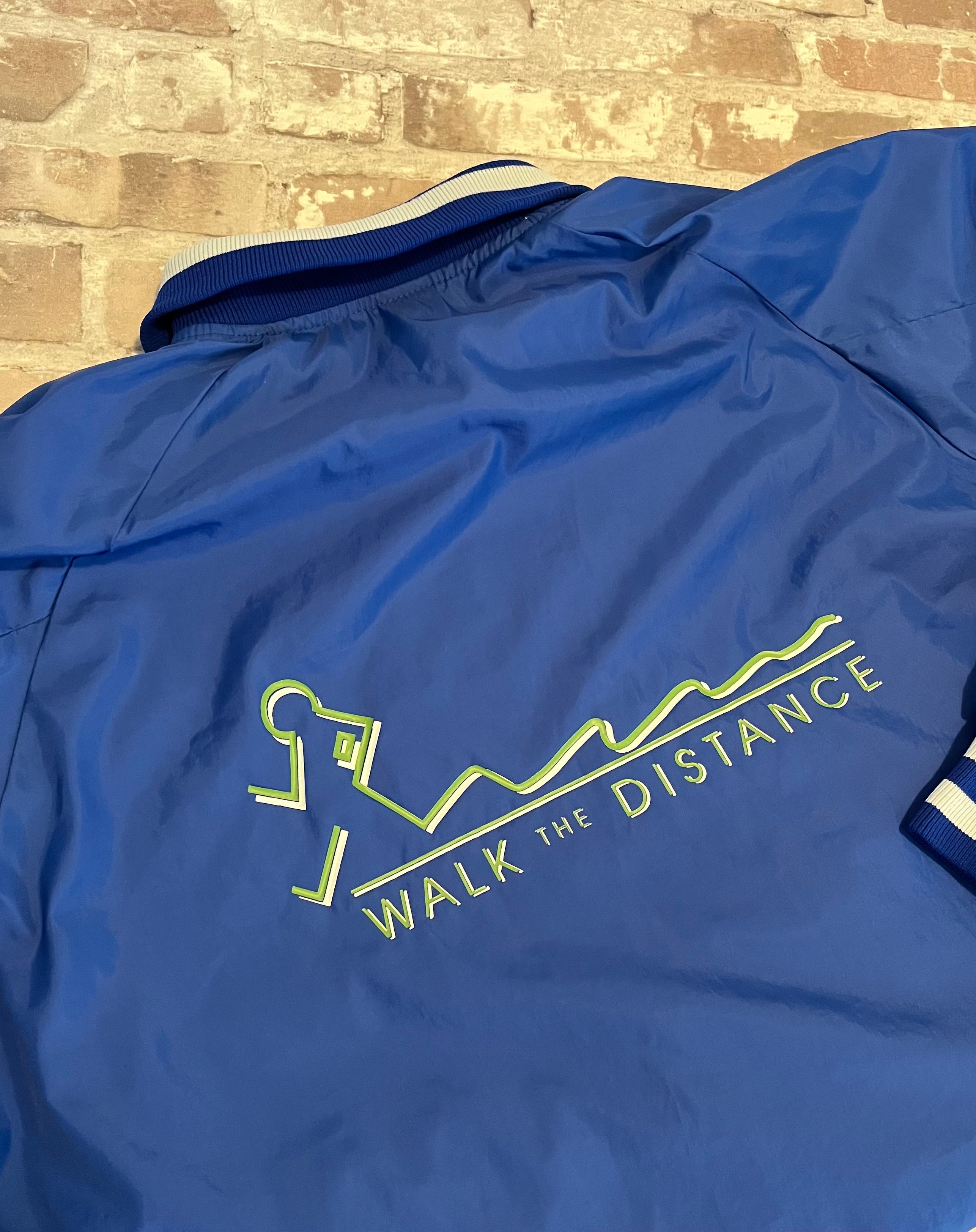 Veste de sport pullover vintage Glaxo bleu roi avec col polo zippé, bords-côtes rayés et sérigraphie sur la poitrine, présentée à plat, de dos.