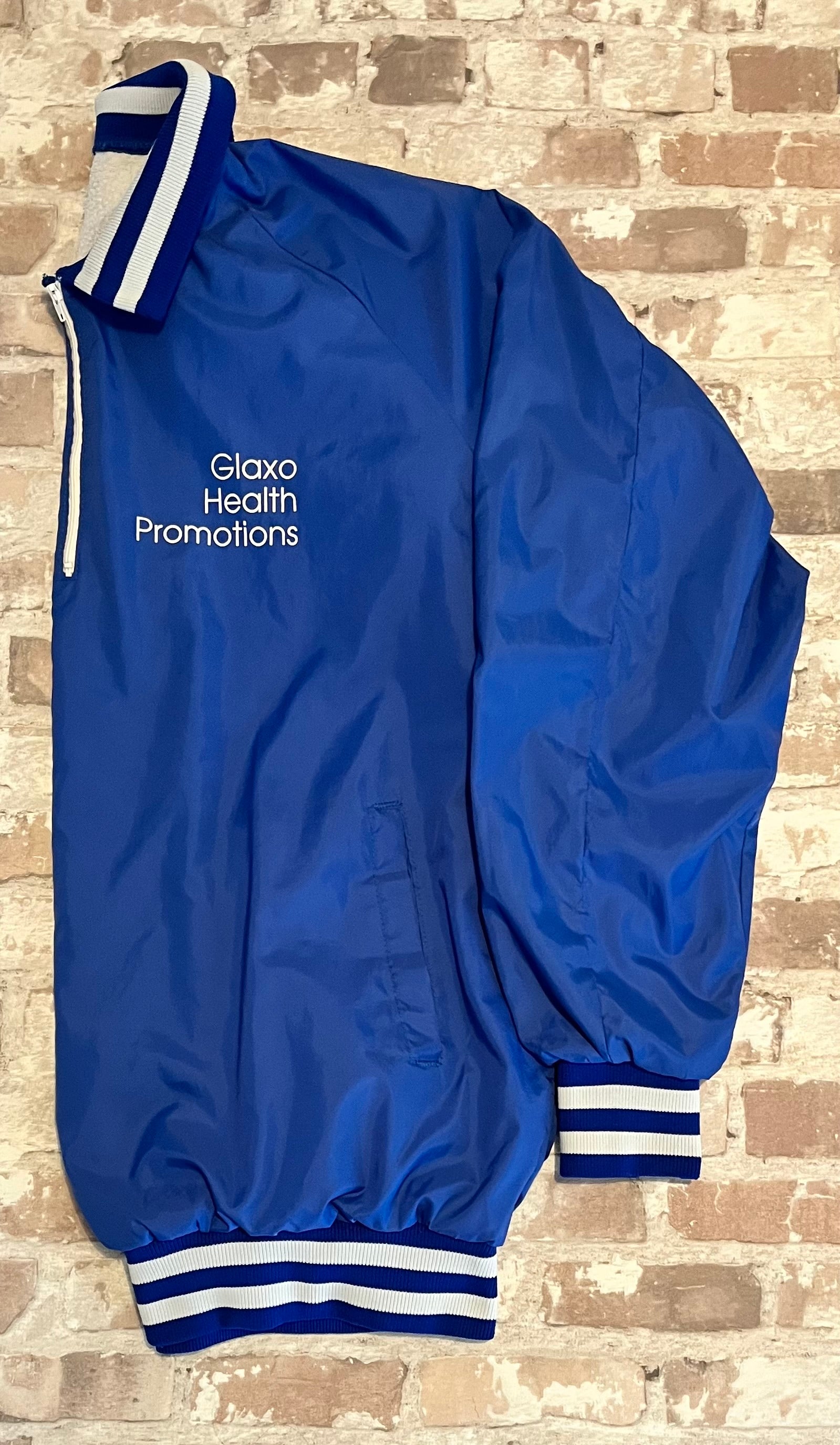 Veste de sport pullover vintage Glaxo bleu roi avec col polo zippé, bords-côtes rayés et sérigraphie sur la poitrine, présentée à plat, de profil