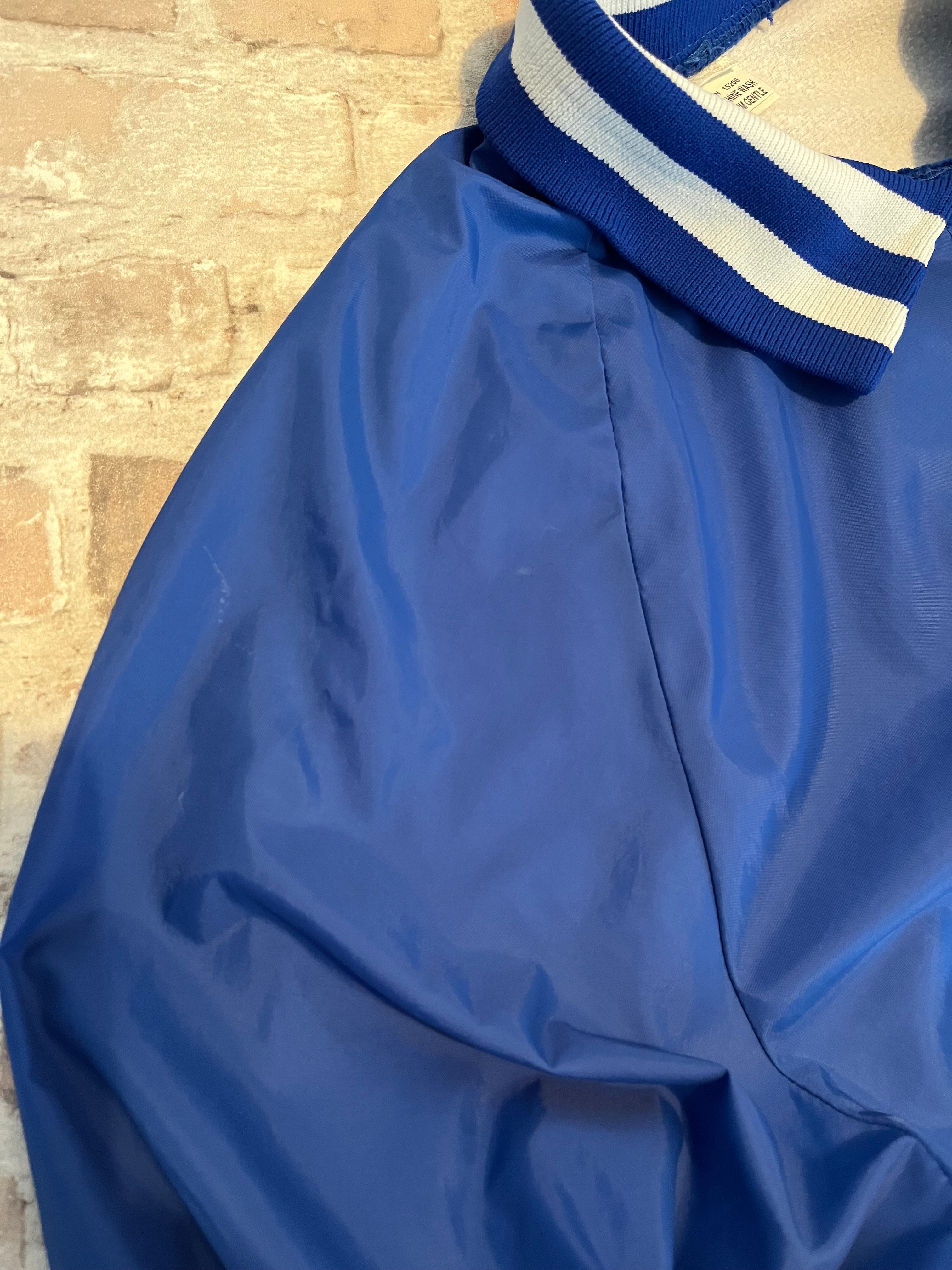 Veste de sport pullover vintage Glaxo bleu roi avec col polo zippé, bords-côtes rayés et sérigraphie sur la poitrine, présentée à plat, focus taches