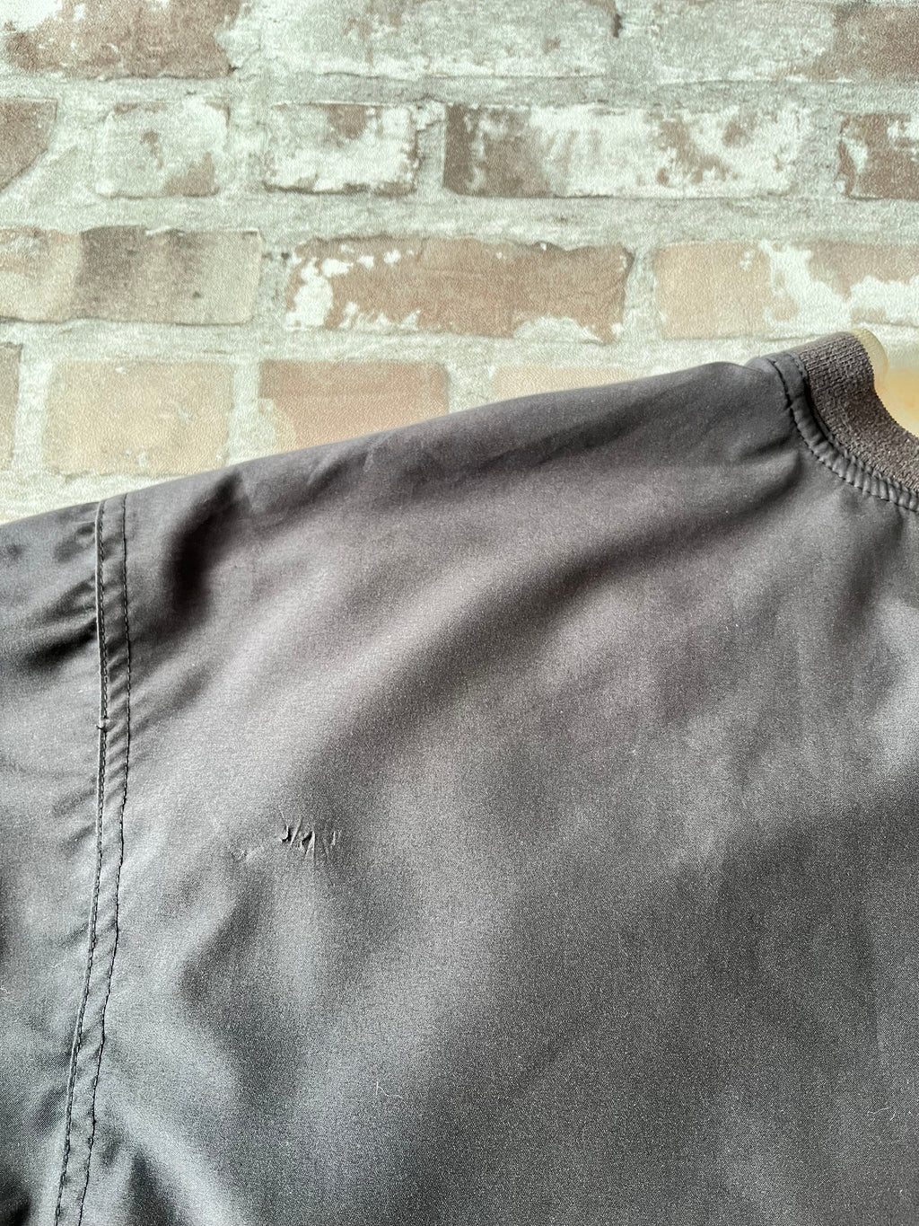 Veste de sport pullover vintage LA Loving noire au toucher peau de pêche avec broderie Buffalo et col en V marron, présentée à plat. Focus Accroc dos.