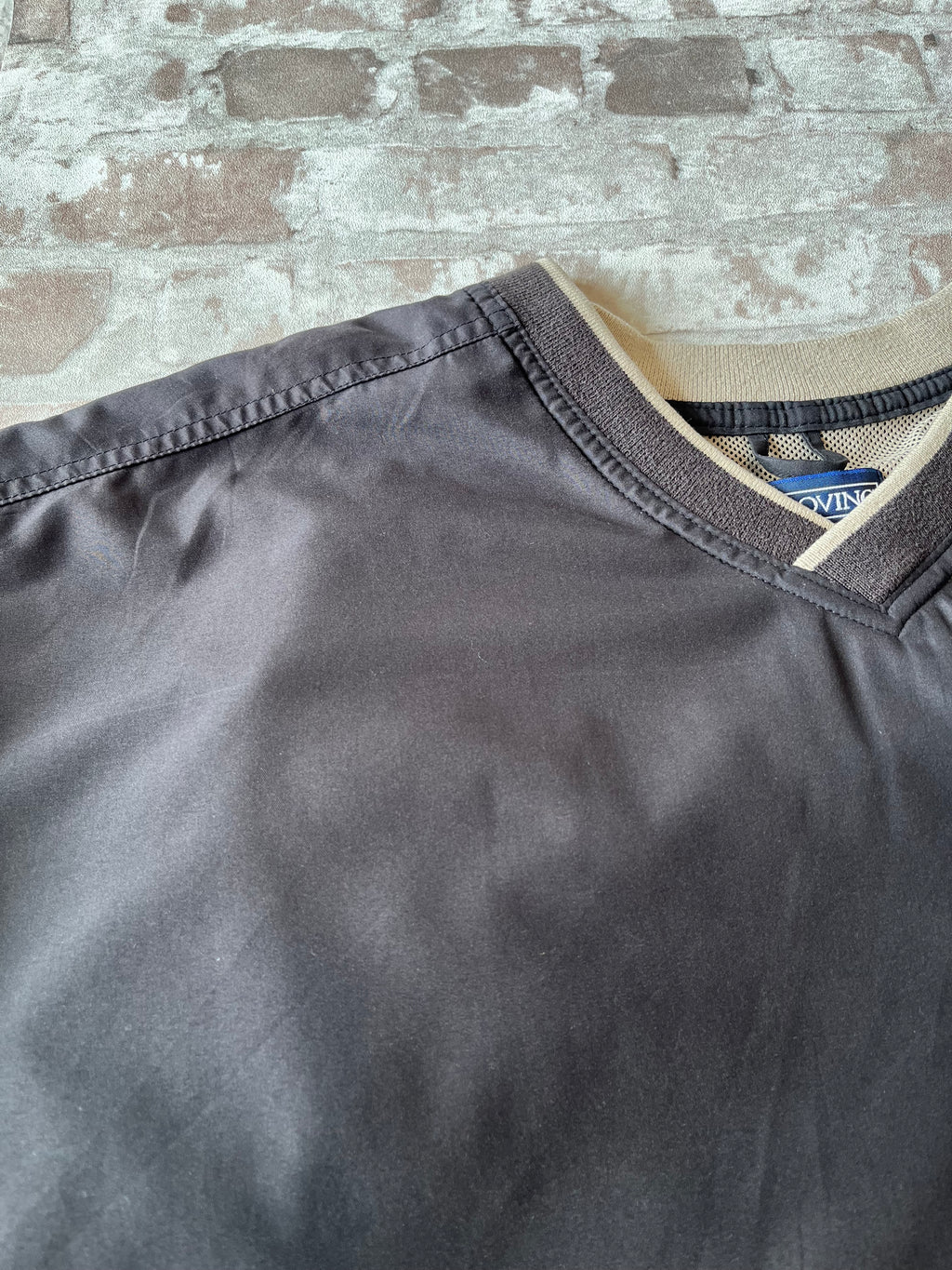 Veste de sport pullover vintage LA Loving noire au toucher peau de pêche avec broderie Buffalo et col en V marron, présentée à plat. Focus marque/pli discret horizontal