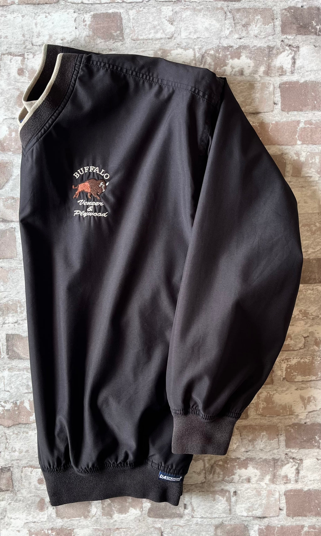 Veste de sport pullover vintage LA Loving noire au toucher peau de pêche avec broderie Buffalo et col en V marron, présentée à plat, de profil